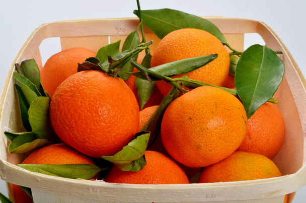 Szerves mandarin zöld levelekkel, fa kosárban, fehér alapon - Fotó, kép