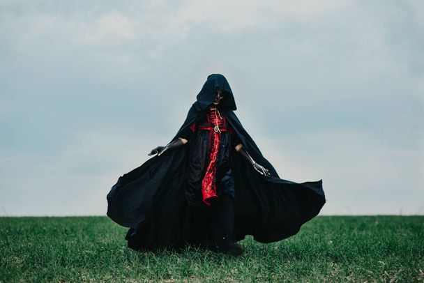 Fiatal nő sétál át a mezőn Halloween jelmezben a halál festett csontváz a testén ellen háttér ég. Halloween koncepció. Cukor koponya smink. - Fotó, kép