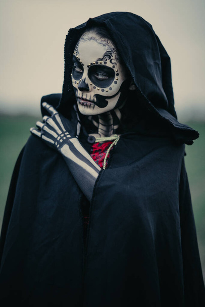 Portrét mladé ženy v halloweenském kostýmu smrti s namalovanou kostrou na těle a nalíčenou cukrovou lebkou. Halloween koncept. - Fotografie, Obrázek