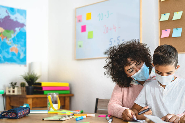 Teacher woman with child wearing face protective mask in preschool classroom during corona virus pandemic - Healthcare and education concept - Photo, Image