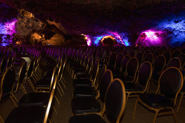 Gekleurde stoelen in de grot voor het concert. Stoelen in de concertzaal. Lege rijen rode stoelen in de grot. Gekleurde scène. - Foto, afbeelding