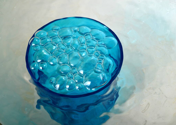 Agua desbordante en un vaso azul, vidrio desbordante lleno de agua y burbujas - Foto, imagen