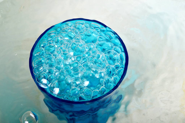 Agua desbordante en un vaso azul, vidrio desbordante lleno de agua y burbujas - Foto, imagen
