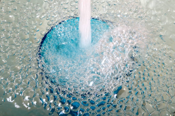 Agua desbordante en un vaso azul, vidrio desbordante lleno de agua y burbujas - Foto, Imagen