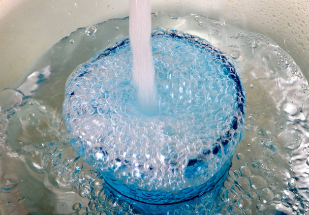 Overstromend water in een blauw glas, volledig overstromend glas met water en bellen - Foto, afbeelding