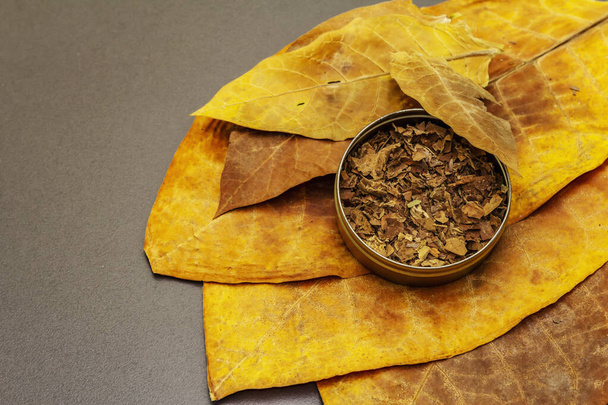 Geraspte tabak in een blikken doos. Hoge kwaliteit genezen grote bladeren om sigaren te maken. Zwarte steen beton achtergrond, kopieer ruimte - Foto, afbeelding