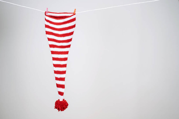 Une casquette rayée rouge et blanche avec une longue queue et un grand pompon rouge accroché à une corde blanche sur un fond blanc. - Photo, image