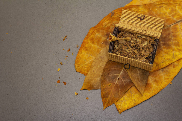 Roztrhaný tabák v proutěné truhlici. Vysoce kvalitní nasolené velké listy na výrobu doutníků. Černý kámen betonové pozadí, horní pohled - Fotografie, Obrázek