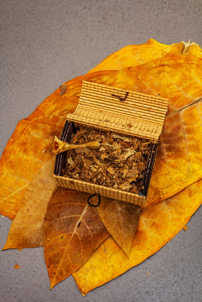 Подрібнений тютюн у плетеній грудній клітці. Високоякісні вилікувані великі листя для виготовлення сигар. Чорний кам'яний бетонний фон, вид зверху
 - Фото, зображення