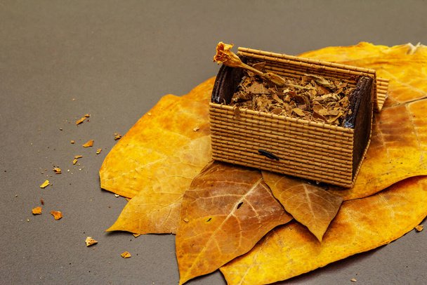 Geschredderter Tabak in einer Korbtruhe. Hochwertig gehärtete große Blätter zur Herstellung von Zigarren. Schwarzer Stein Betonhintergrund, Kopierraum - Foto, Bild