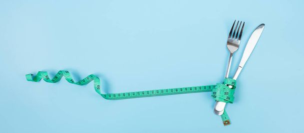 トップ表示緑青の背景にフォークとナイフを包んだ測定テープ。ダイエット、減量、肥満、食品管理の概念は - 写真・画像