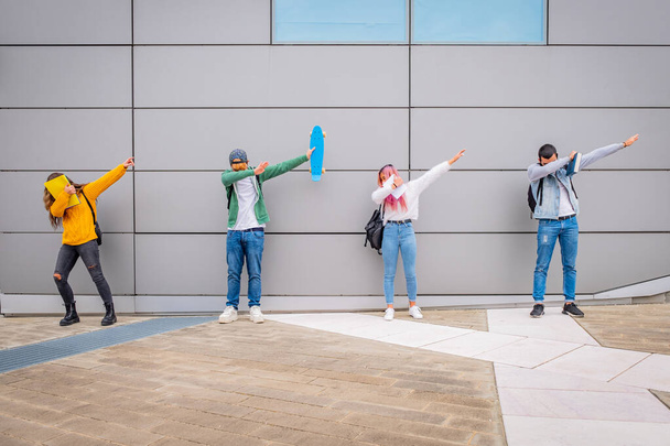 Πολυεθνικοί νέοι που χορεύουν το χορό dab υπαίθρια κρατώντας την κοινωνική απόσταση κατά την περίοδο του coronavirus - παιχνιδιάρηδες μαθητές που κάνουν αστείες πόζες με προστατευτική μάσκα για την πρόληψη της εξάπλωσης των ιών - Φωτογραφία, εικόνα