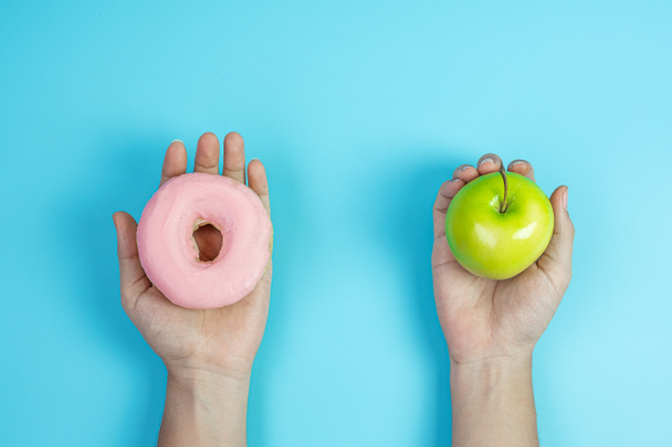 Frau mit grünem Apfel und rosa Donut, weibliche Wahl zwischen Obst ist gesundes Essen und süß ist ungesundes Junk Food. Ernährung, Fettleibigkeit, Lebensstil und Ernährungskonzept - Foto, Bild