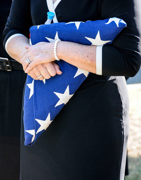 A mourner clutches a folded American flag at the military funeral of a loved onel - Фото, изображение