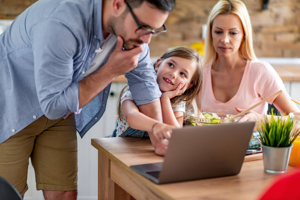 Famiglia giovane che utilizza il computer portatile in cucina, alla ricerca di ricette alimentari sane. - Foto, immagini