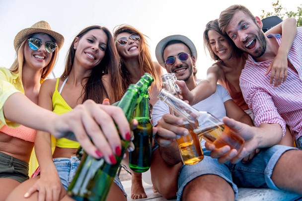 休暇中の友人のグループは、ビールで乾杯しながらプールでパーティーをしています。休暇、友人やライフスタイルの概念. - 写真・画像