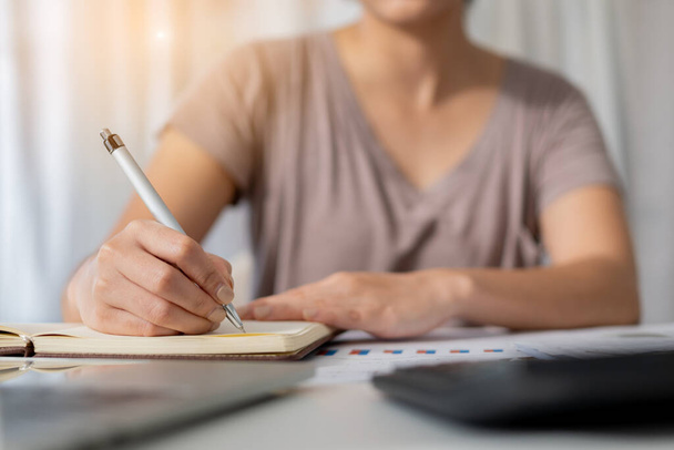 Gros plan femme étudiante main écrit carnet avec ordinateur portable à la maison - Photo, image
