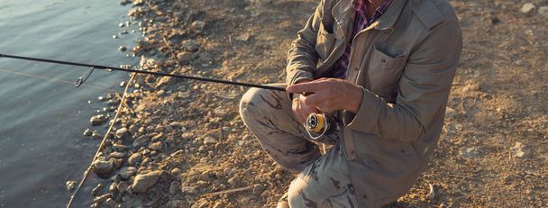 Fishing rod τροχό closeup, ο άνθρωπος αλιείας με ένα όμορφο ηλιοβασίλεμα. - Φωτογραφία, εικόνα