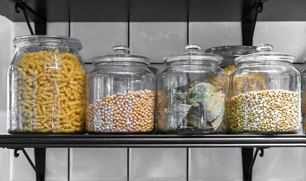 Кухонные стеклянные банки с зерновыми, макаронами и лавровыми листьями. - Фото, изображение