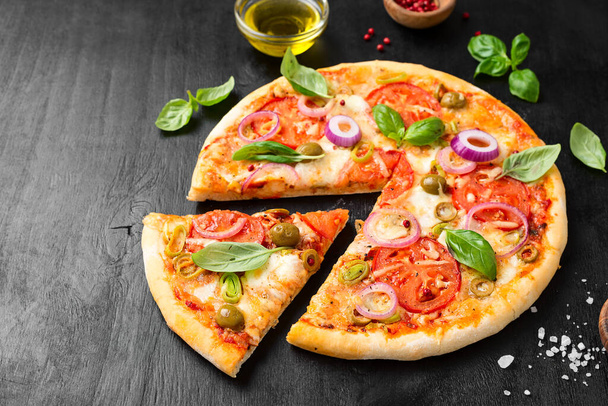 Pizza italiana con queso mozzarella derretido aceitunas verdes y tomate adornado con verduras frescas y hojas de albahaca. - Foto, Imagen