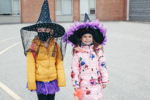 Mutlu Cadılar Bayramı. Çocuklar, kostümlü kızlar ve okula giderken koruyucu maskelerle karşılaşıyorlar. Cadılar Bayramı 'nı kutlayan okul öğrencileri. Koronavirüs sırasında yeni bir normal.. - Fotoğraf, Görsel