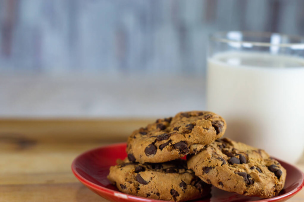 Csokoládé Chip cookie-k piros tányéron és tej fa asztalon - másolás terület - Fotó, kép
