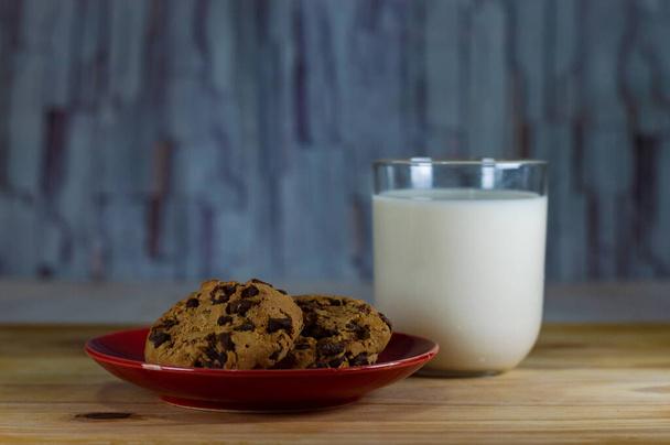 チョコレートチップクッキーは、木製のテーブルの上に赤いプレートとミルク-コピースペースエリア - 写真・画像