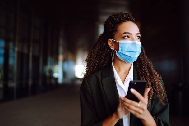 Beautiful businesswoman in medical protective mask using the phone. Safety during coronavirus pandemic, epidemic covid-19. - Foto, Imagem