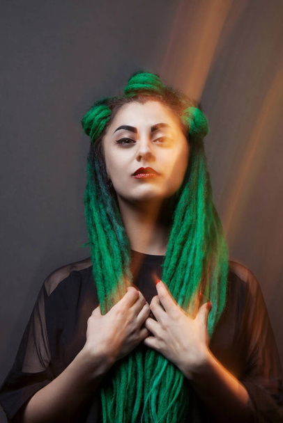 Pretty girl with green long dreadlocks. Black background. Mixed light. - Фото, изображение