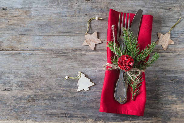 Mesa festiva para la cena navideña. Tenedor y cuchillo vintage, servilleta roja y decoraciones navideñas sobre fondo de madera vieja. vista superior, espacio de copia - Foto, imagen