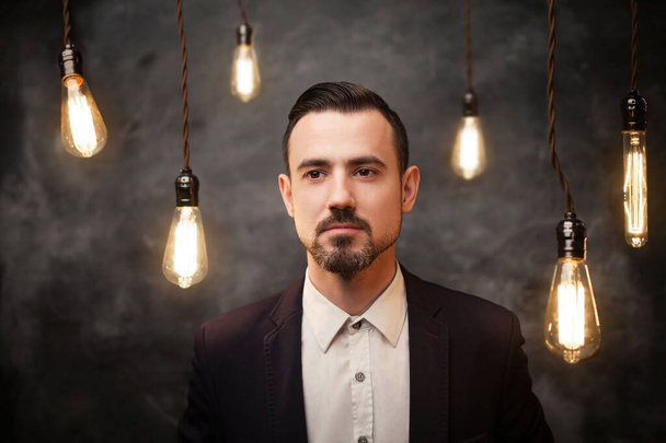 Portrait of a young bearded man. Gray background with edison lamps. - Foto, Imagen