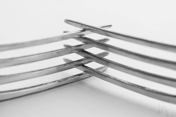 Closeup of the crossed tines of two forks. White background, selective focus - Foto, Imagem