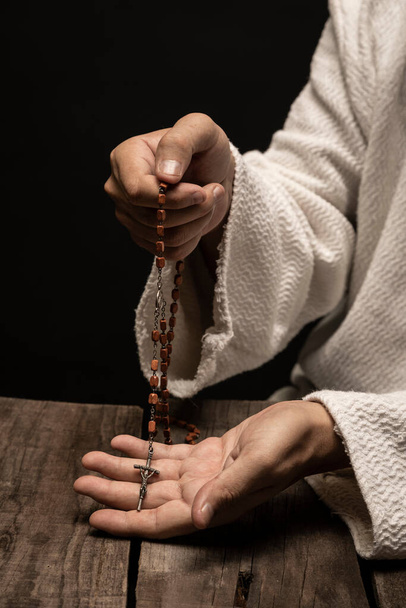 Jesus Christ praying to God with the Holy Rosary in hands in the dark black night - Фото, изображение