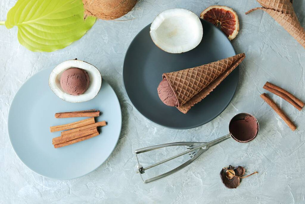 Домашнее шоколадное мороженое в вафельных рожках, кокосы на светлом столе, вид сверху, домашняя кухня, здоровая еда - Фото, изображение