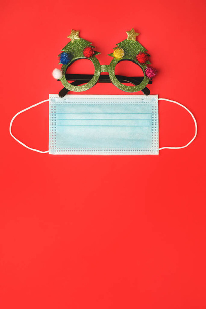 Рождественские очки с защитной хирургической маской на красном фоне - Фото, изображение