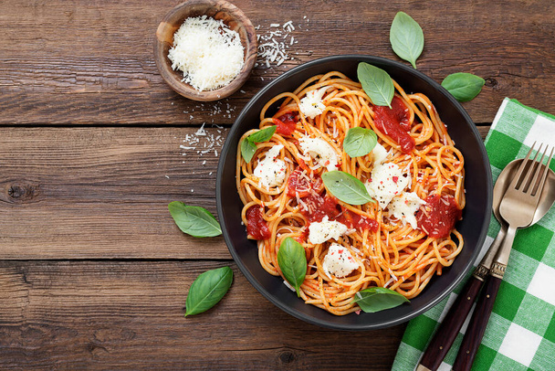 Спагетті з томатним соусом, пармезаном та сиром моцарелла, прикрашеним базиліком
. - Фото, зображення