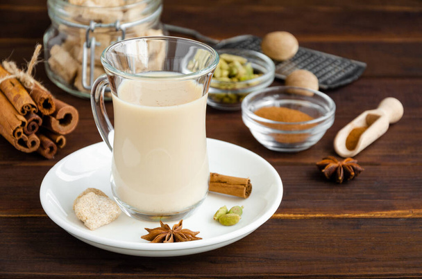 Heißer Tee mit Milch, Zimt, Kardamom, Anis und anderen Gewürzen, indischer Masala-Tee in einer Glasschale auf Holzgrund. Kopierraum - Foto, Bild