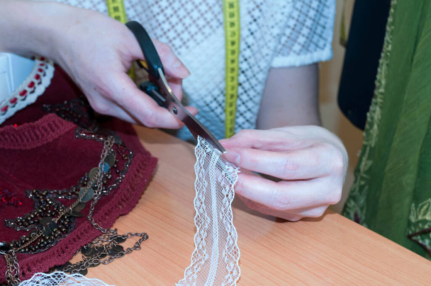 partial view of tailor cutting white lace with scissors on wooden table in sawing studio - Zdjęcie, obraz