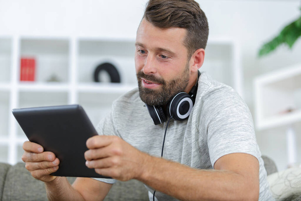 man on sofa with headphones using digital tablet - Photo, image