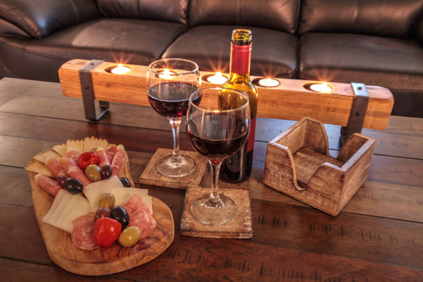 プロシクト・パニーノ、モッツァレラチーズ、ジェノヴァサラミ、フォンティーナチーズ、職人クラッカーの広がりの背後にキャンドルのある素朴な木の上にシャルキュトリボードと赤ワイン. - 写真・画像