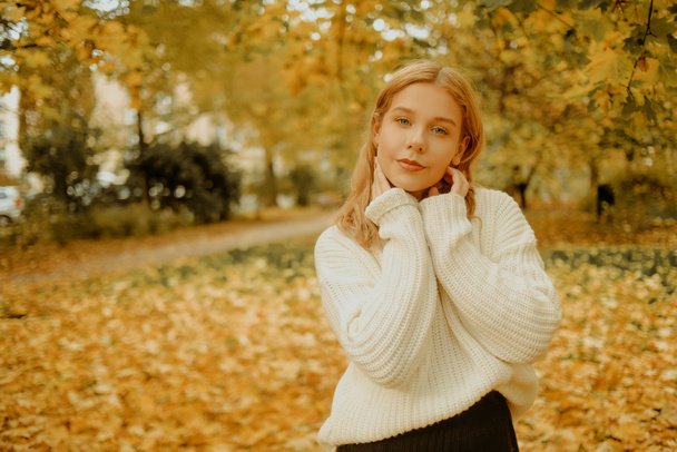 Женщина в осеннем парке. Девочка-подросток на фоне осенних листьев. Модное фото модели в белом тёплом свитере. Блондинка смотрит в камеру - Фото, изображение