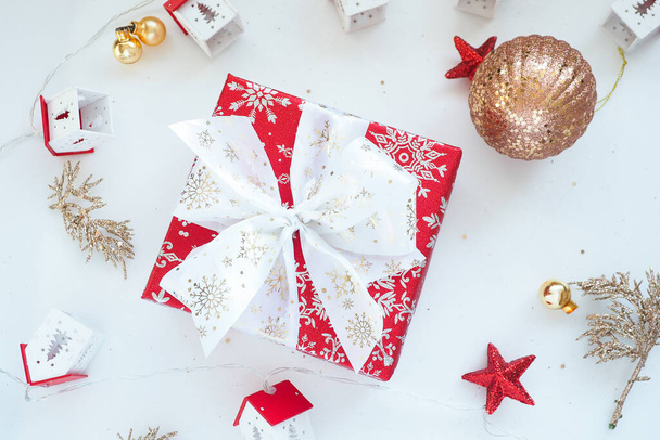 punainen lahjapakkaus, jossa valkoinen jousi, joulupallot ja koristetalot valkoisella taustalla - Valokuva, kuva