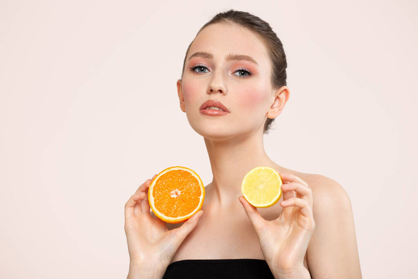 Piękna kobieta z czystą skórą trzyma w dłoniach połówki pomarańczy i młodą cytrynę. Pielęgnacja ciała i twarzy - Zdjęcie, obraz