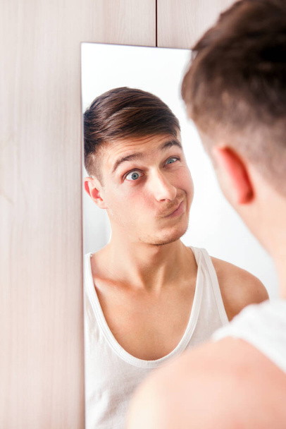 Young Man looking to Reflection in the Mirror and make a Funny Face - Fotó, kép
