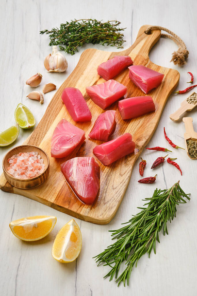 Fresh pieces of tuna fillet with spice and herbs on wooden cutting board - Фото, изображение