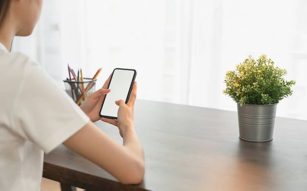 Mujer joven de la mano sosteniendo el teléfono inteligente sobre la mesa y la pantalla está en blanco, concepto de red social. - Foto, imagen