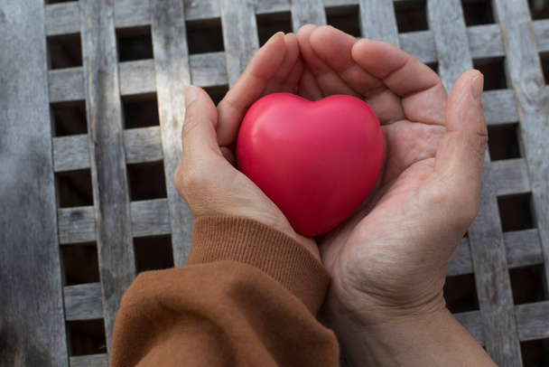 handen houden een rood hart in de houten achtergrond - Foto, afbeelding