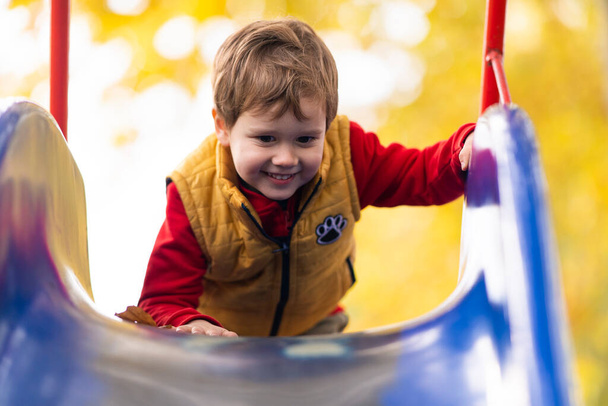Happy smiling child boy climbing on a frame/ slide at an outdoors playground. - Φωτογραφία, εικόνα