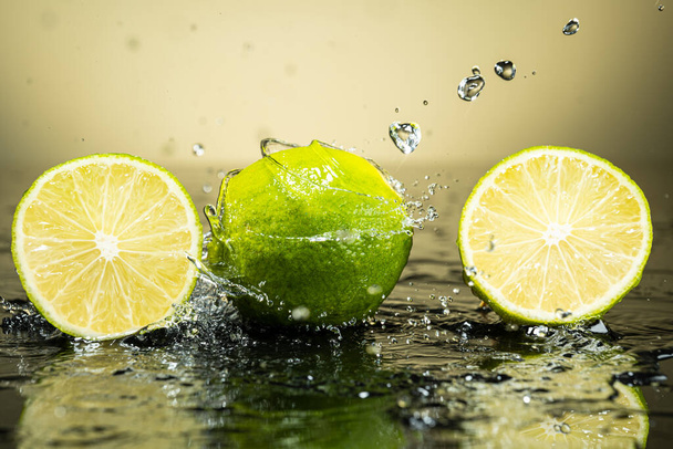 Two green limes on gradient background with splash and water drops - Фото, изображение