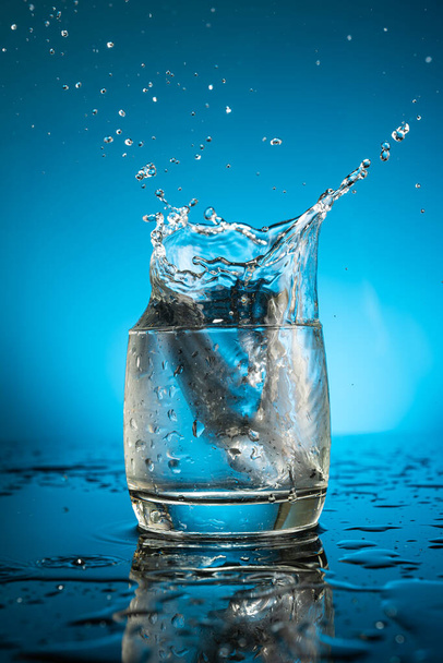 Splash in a glass of water from a falling piece of ice on a blue background - Fotó, kép